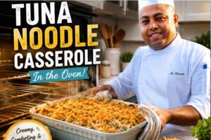 A smiling chef in a white uniform holds a freshly baked tuna noodle casserole in a casserole dish beside an open oven in a modern kitchen. Large text reads “Tuna Noodle Casserole in the Oven,” highlighting the creamy, golden-brown baked pasta dish as a comforting family meal.