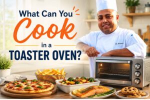 Smiling chef in a white uniform standing beside a toaster oven in a bright kitchen, surrounded by pizza, fries, roasted vegetables, salmon, and cookies, with the text "What Can You Cook in a Toaster Oven?" displayed prominently.