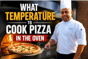 Professional chef standing beside a wood-fired pizza oven holding a freshly baked pizza, with large text reading “What Temperature to Cook Pizza in the Oven.” The feature image showcases a hot pizza oven, golden pizza crust, and a modern kitchen setting, ideal for a pizza baking guide.
